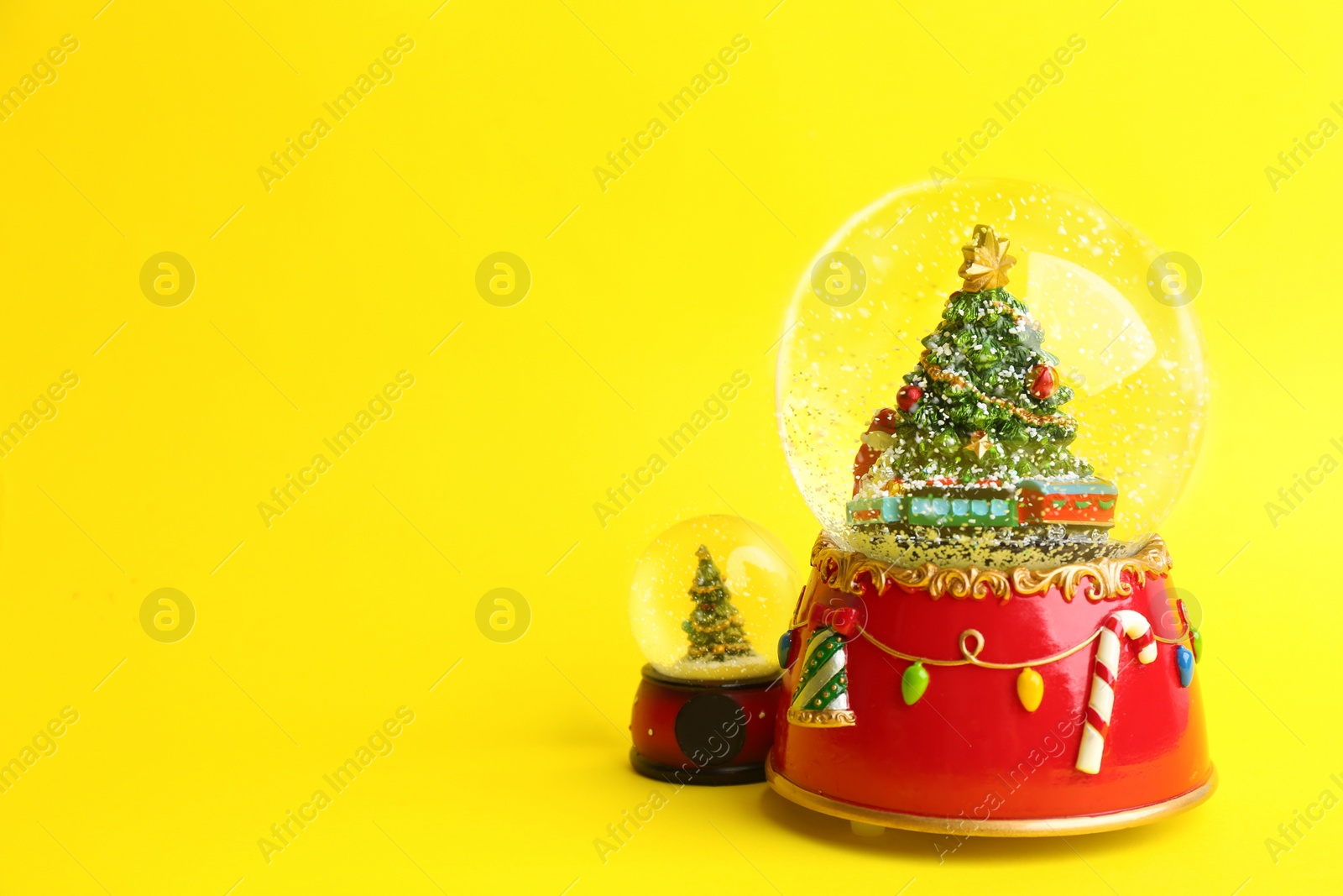 Beautiful snow globes with Christmas trees on yellow background, space for text Photo of Beautiful snow globes with Christmas trees on yellow background, space for text