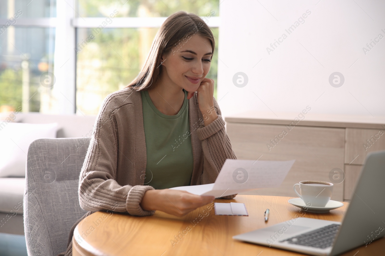 Woman reading letter at wooden table in room Photo of Woman reading letter at wooden table in room
