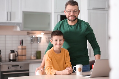 Photo of Little boy and his dad using laptop in kitchen