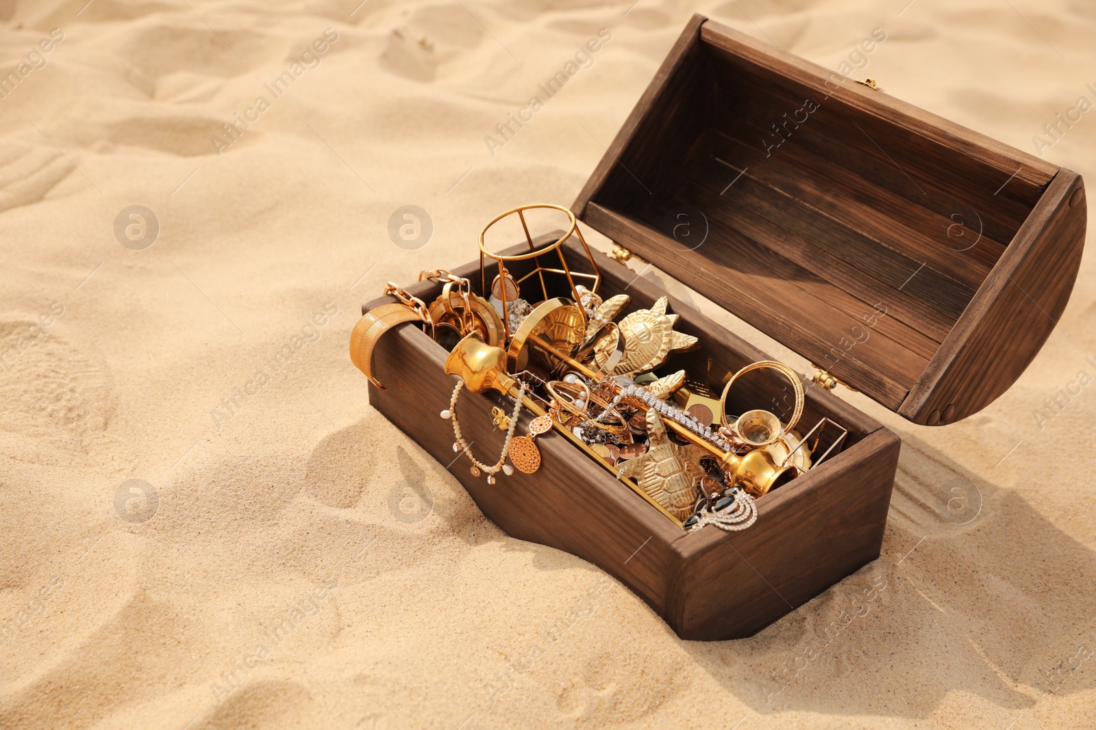 Open wooden chest with treasures on sand, space for text Photo of Open wooden chest with treasures on sand, space for text