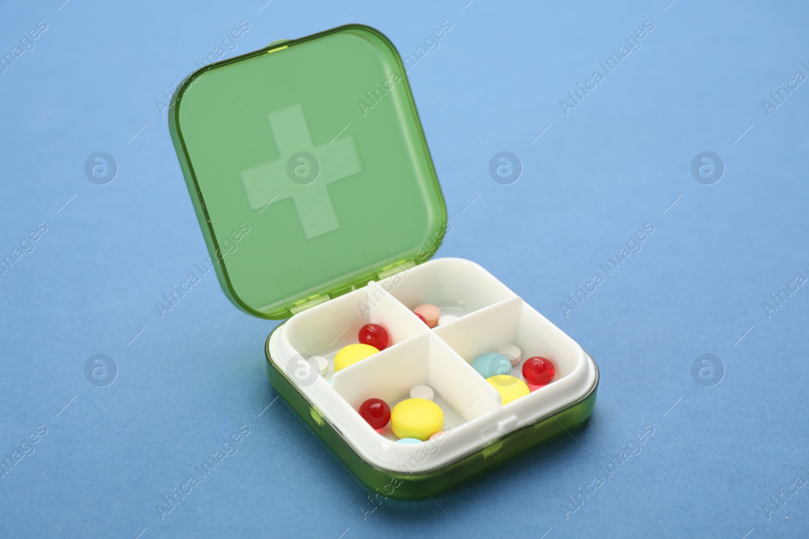Plastic box with different pills on light blue background Photo of Plastic box with different pills on light blue background