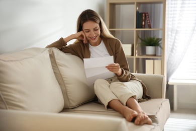 Happy woman reading letter on sofa at home Photo of Happy woman reading letter on sofa at home