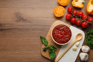 Delicious adjika sauce in bowl and ingredients on wooden table, flat lay. Space for text Photo of Delicious adjika sauce in bowl and ingredients on wooden table, flat lay. Space for text