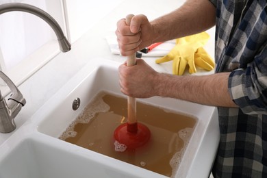 Man using plunger to unclog sink drain in kitchen, closeup Photo of Man using plunger to unclog sink drain in kitchen, closeup