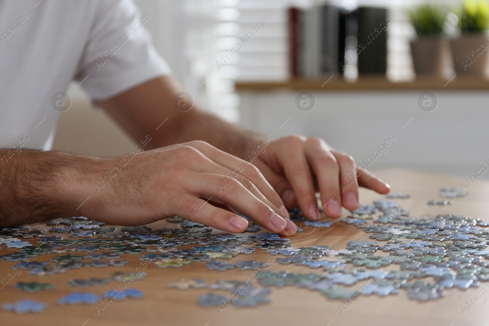 Man playing with puzzles at wooden table indoors, closeup Photo of Man playing with puzzles at wooden table indoors, closeup