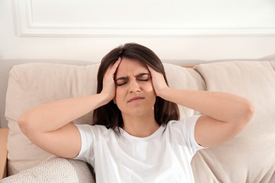Young woman suffering from migraine on sofa at home Photo of Young woman suffering from migraine on sofa at home
