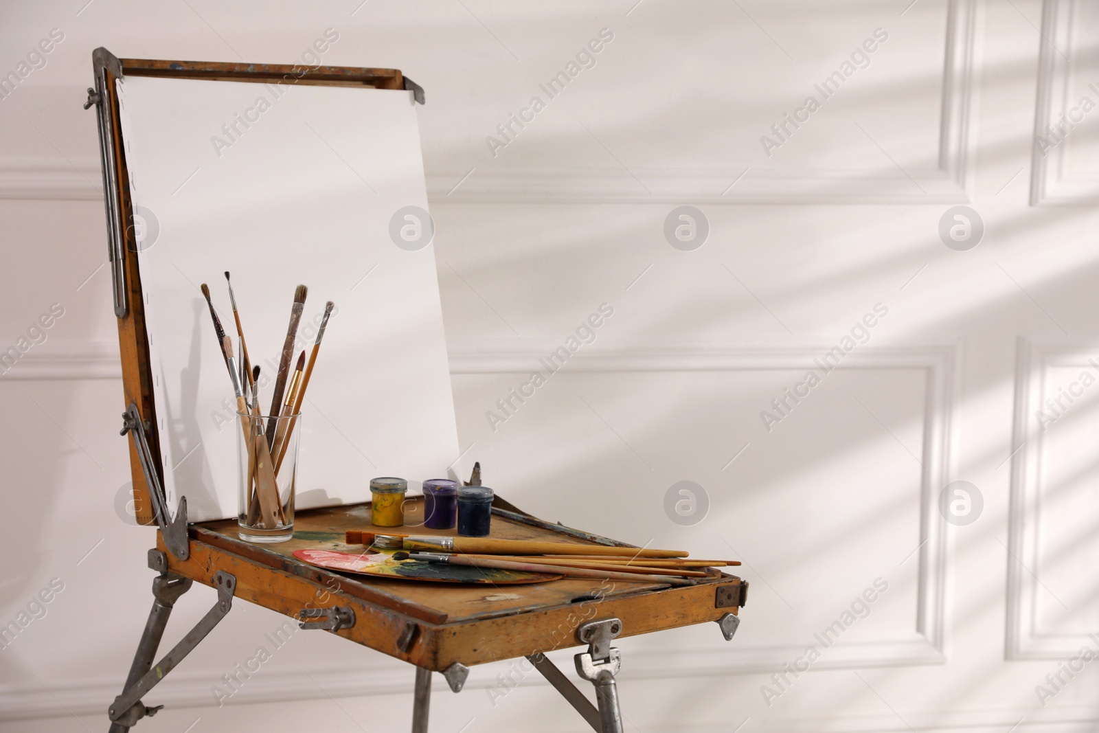 Photo of Easel with blank canvas, palette and brushes in art studio. Space for text