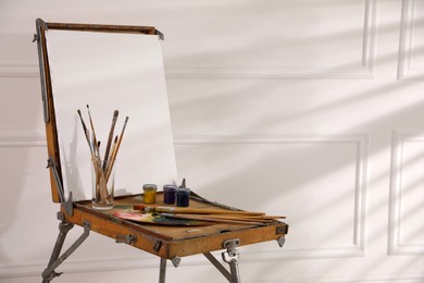 Easel with blank canvas, palette and brushes in art studio. Space for text Photo of Easel with blank canvas, palette and brushes in art studio. Space for text