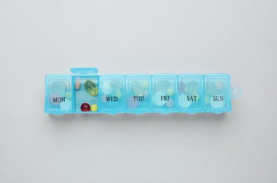 Plastic box with different pills on light grey background, top view Photo of Plastic box with different pills on light grey background, top view