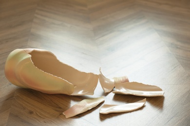 Photo of Broken bright ceramic vase on wooden floor. Space for text
