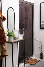 Beautiful fresh potted fern and empty frames on table in hallway Photo of Beautiful fresh potted fern and empty frames on table in hallway