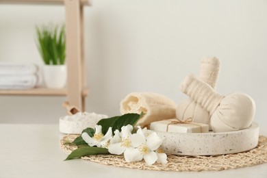 Beautiful jasmine flowers, herbal bags and soap bar on white wooden table indoors, space for text Photo of Beautiful jasmine flowers, herbal bags and soap bar on white wooden table indoors, space for text