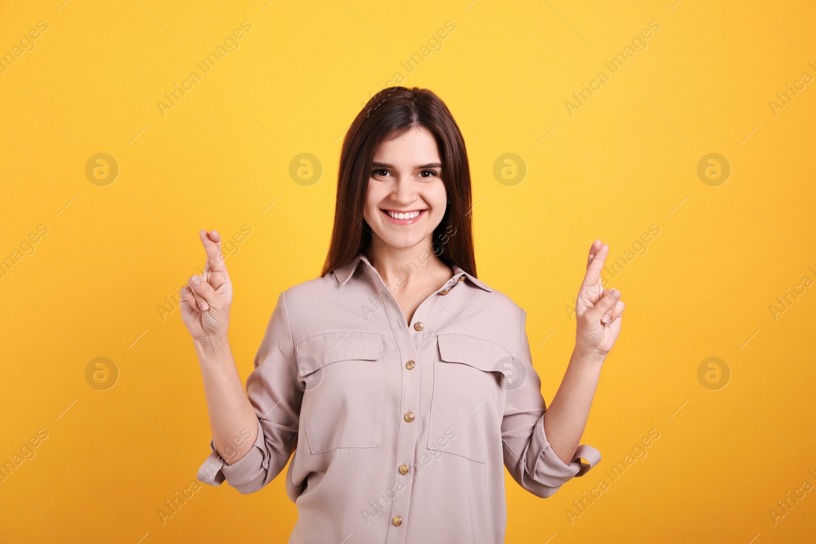 Happy young woman crossing fingers on yellow background. Dealing with stress Photo of Happy young woman crossing fingers on yellow background. Dealing with stress