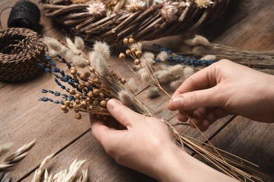 Florist making bouquet of dried flowers at wooden table, closeup Photo of Florist making bouquet of dried flowers at wooden table, closeup