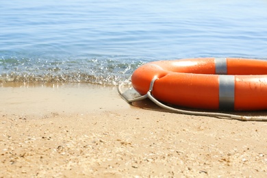 Orange life buoy on sand near sea. Emergency rescue equipment Photo of Orange life buoy on sand near sea. Emergency rescue equipment