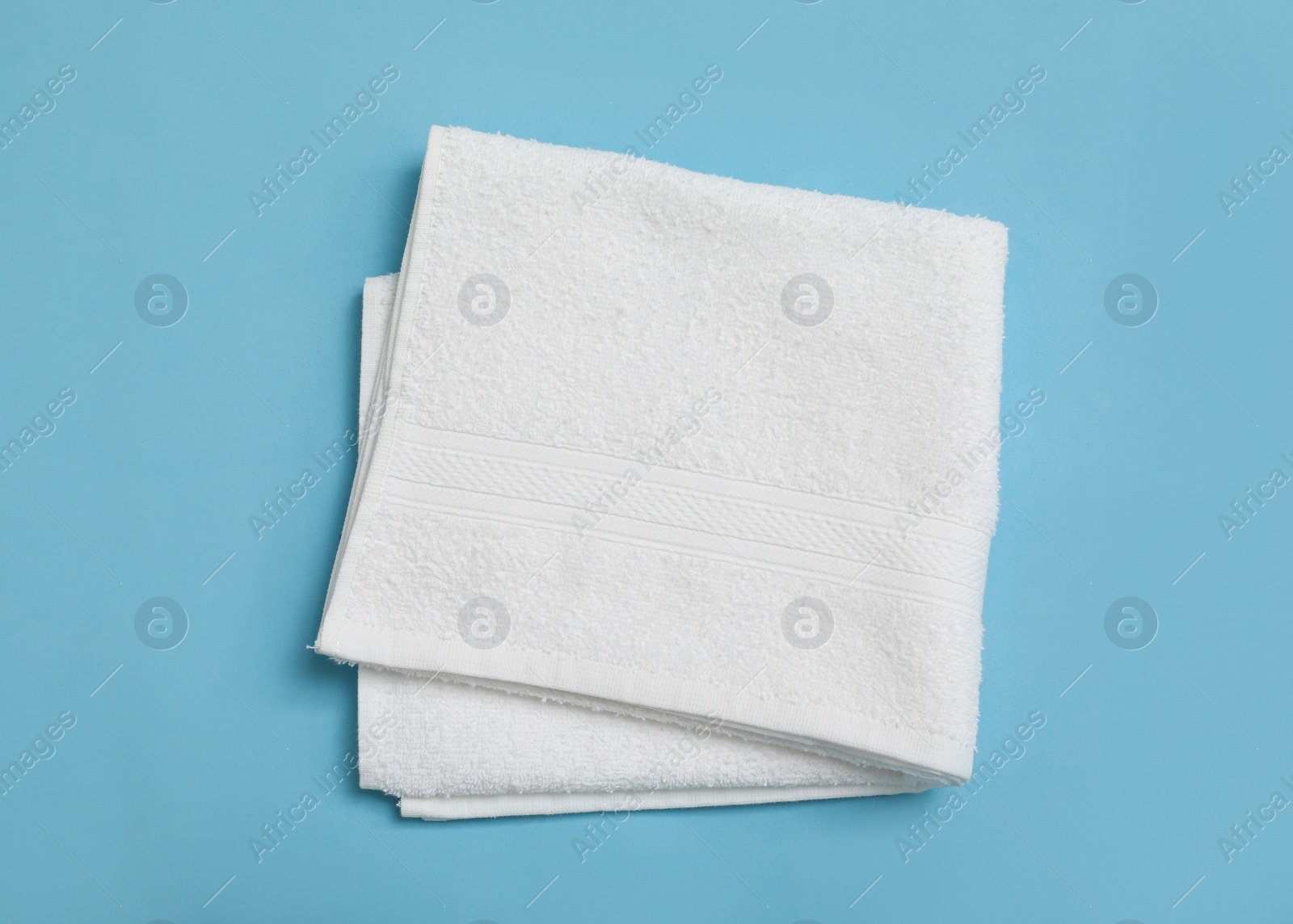 Folded white beach towel on light blue background, top view Photo of Folded white beach towel on light blue background, top view