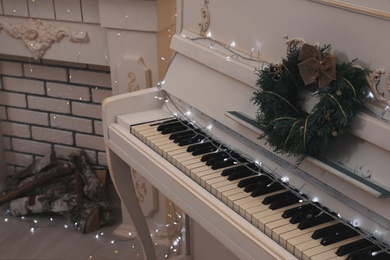 White piano with fairy lights and wreath indoors. Christmas music Photo of White piano with fairy lights and wreath indoors. Christmas music