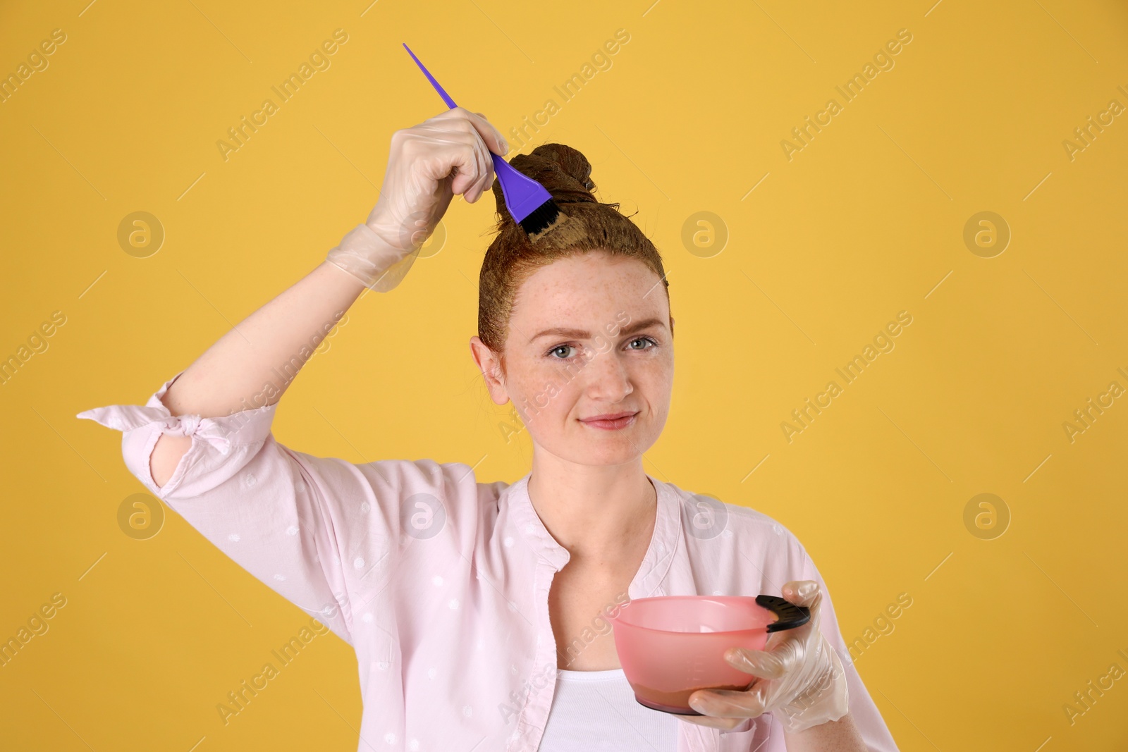Young woman dyeing her hair with henna on yellow background Photo of Young woman dyeing her hair with henna on yellow background