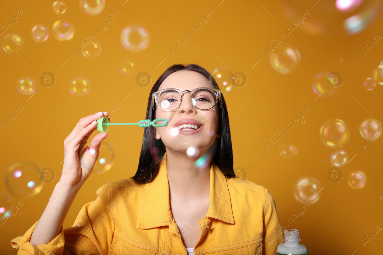 Young woman blowing soap bubbles on yellow background Photo of Young woman blowing soap bubbles on yellow background