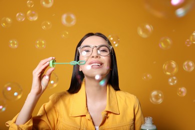 Young woman blowing soap bubbles on yellow background Photo of Young woman blowing soap bubbles on yellow background