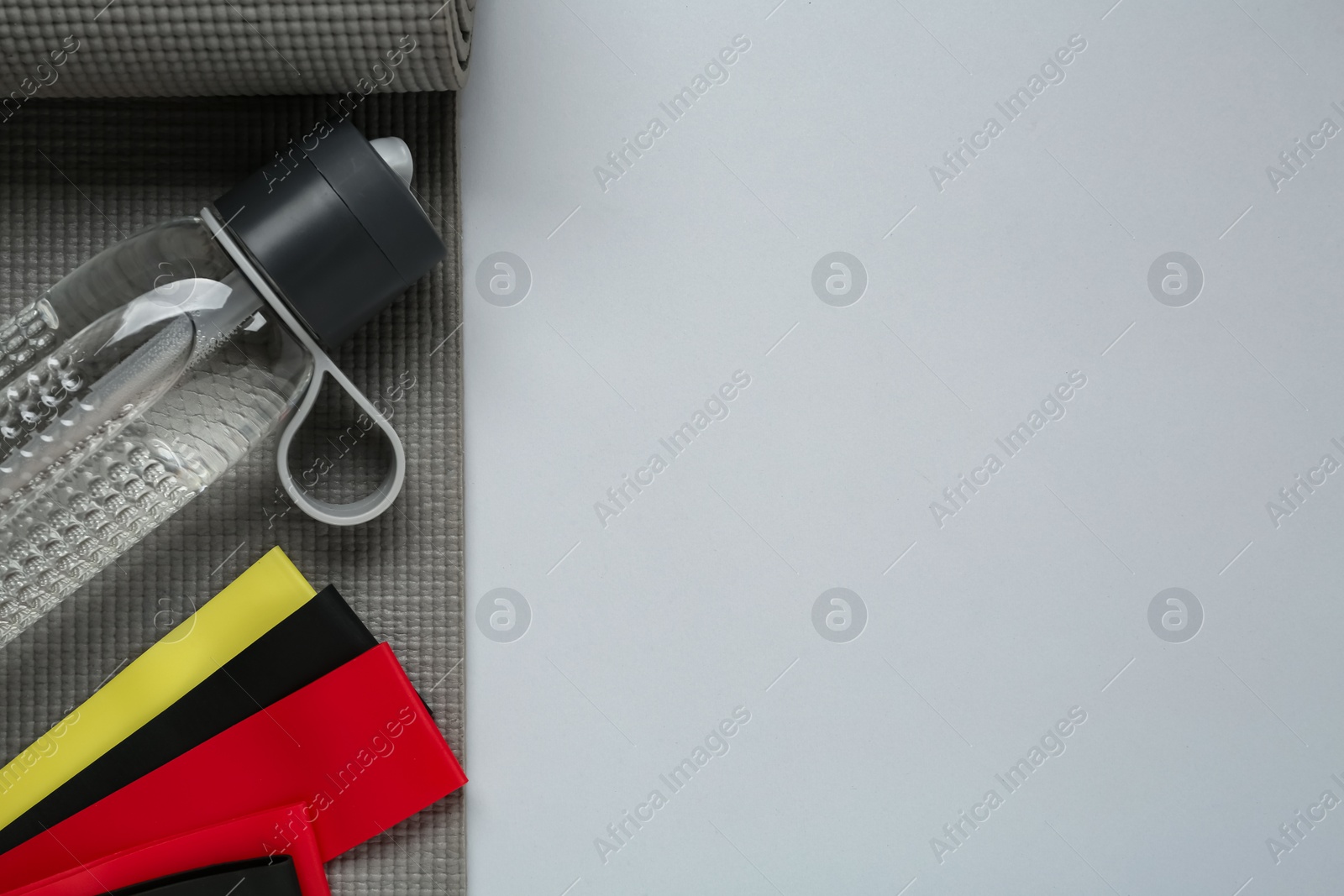 Set of fitness elastic bands, yoga mat and water bottle on grey background, flat lay. Space for text Photo of Set of fitness elastic bands, yoga mat and water bottle on grey background, flat lay. Space for text