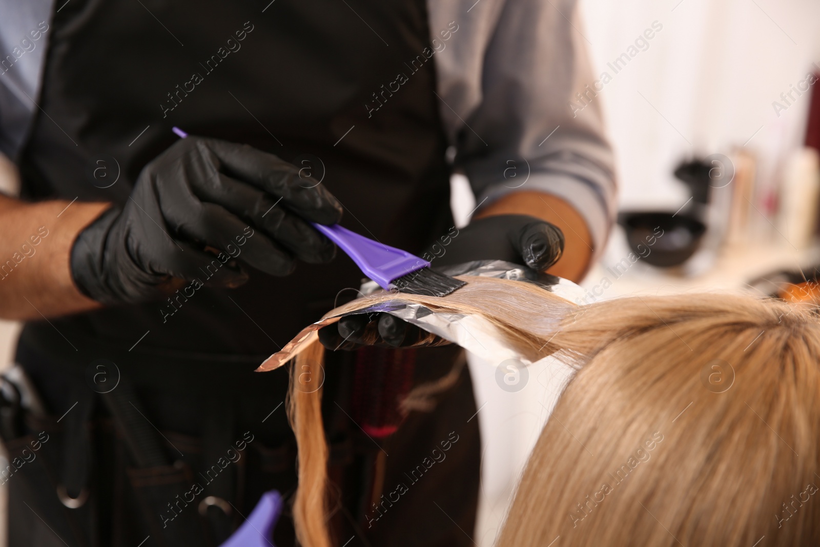 Photo of Professional hairdresser dying hair in beauty salon, closeup