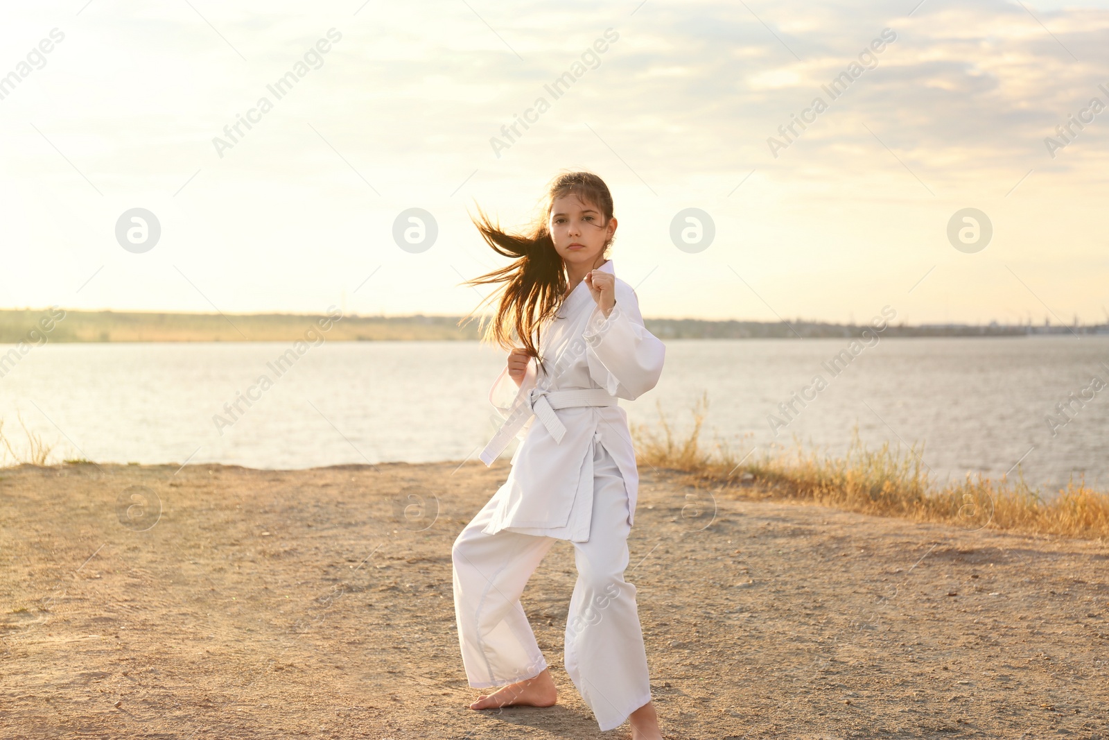 Cute little girl in kimono practicing karate near river on sunny day Photo of Cute little girl in kimono practicing karate near river on sunny day