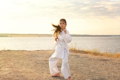 Cute little girl in kimono practicing karate near river on sunny day Photo of Cute little girl in kimono practicing karate near river on sunny day