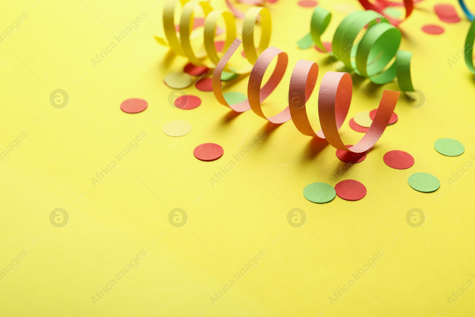 Colorful serpentine streamers and confetti on yellow background. Space for text Photo of Colorful serpentine streamers and confetti on yellow background. Space for text