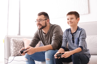 Photo of Little boy and his dad playing video game together at home