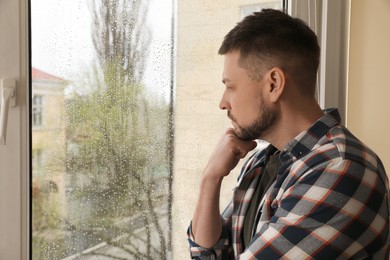 Depressed man near window at home. Space for text Photo of Depressed man near window at home. Space for text