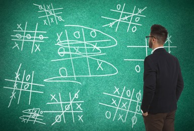 Young businessman near green chalkboard with drawn tic tac toe game Image of Young businessman near green chalkboard with drawn tic tac toe game