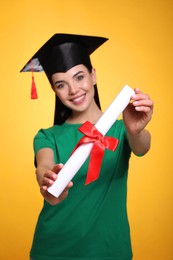 Happy student with graduation hat against yellow background, focus on diploma Photo of Happy student with graduation hat against yellow background, focus on diploma