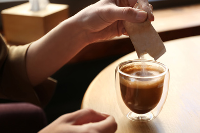 Woman adding sugar to aromatic coffee at table in cafe, closeup Photo of Woman adding sugar to aromatic coffee at table in cafe, closeup