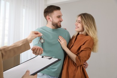 Real estate agent giving key to happy young couple in new house, focus on hands Photo of Real estate agent giving key to happy young couple in new house, focus on hands