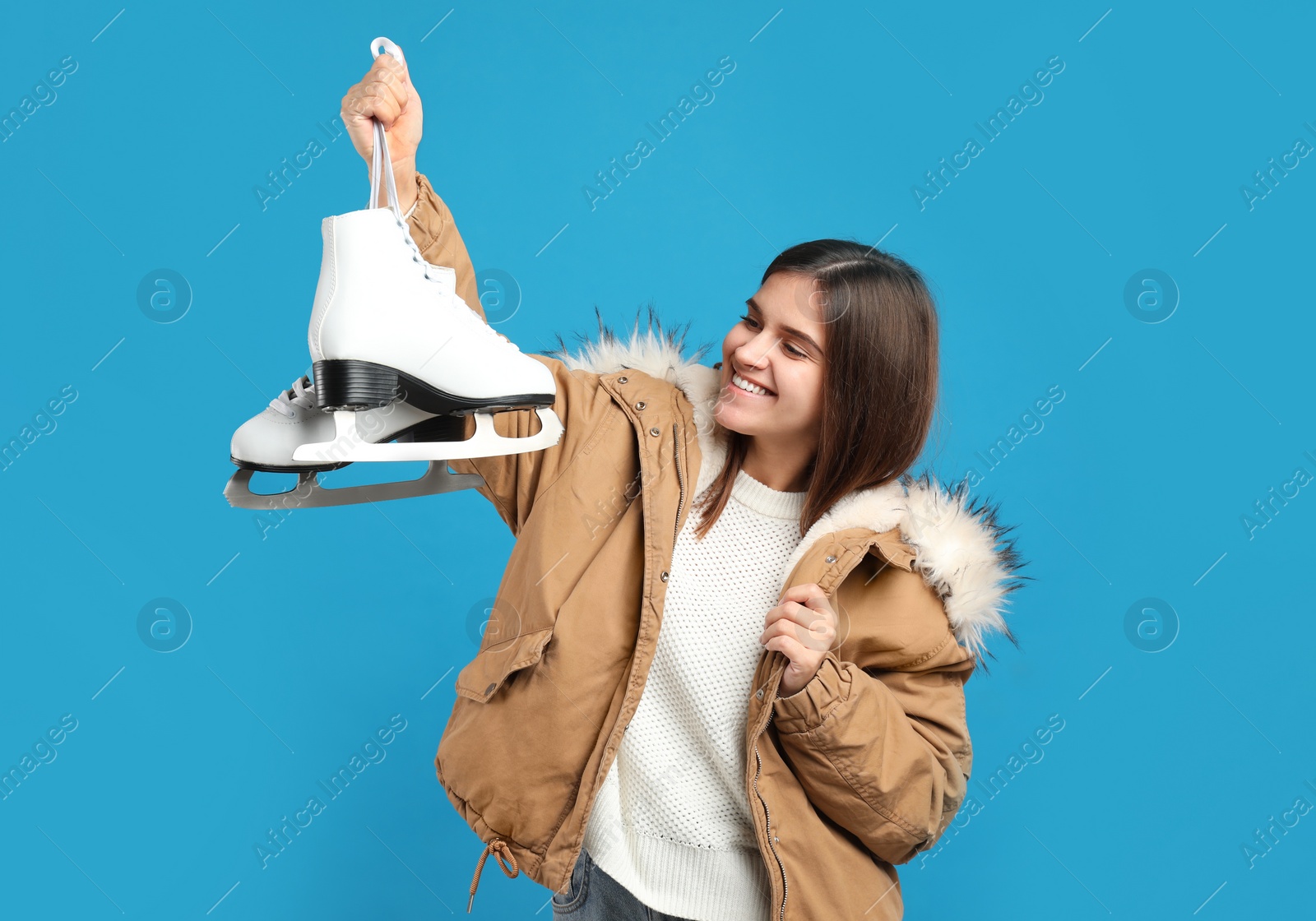 Happy woman with ice skates on light blue background Photo of Happy woman with ice skates on light blue background