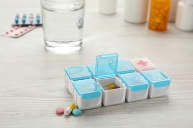 Plastic box with different pills on white wooden table Photo of Plastic box with different pills on white wooden table