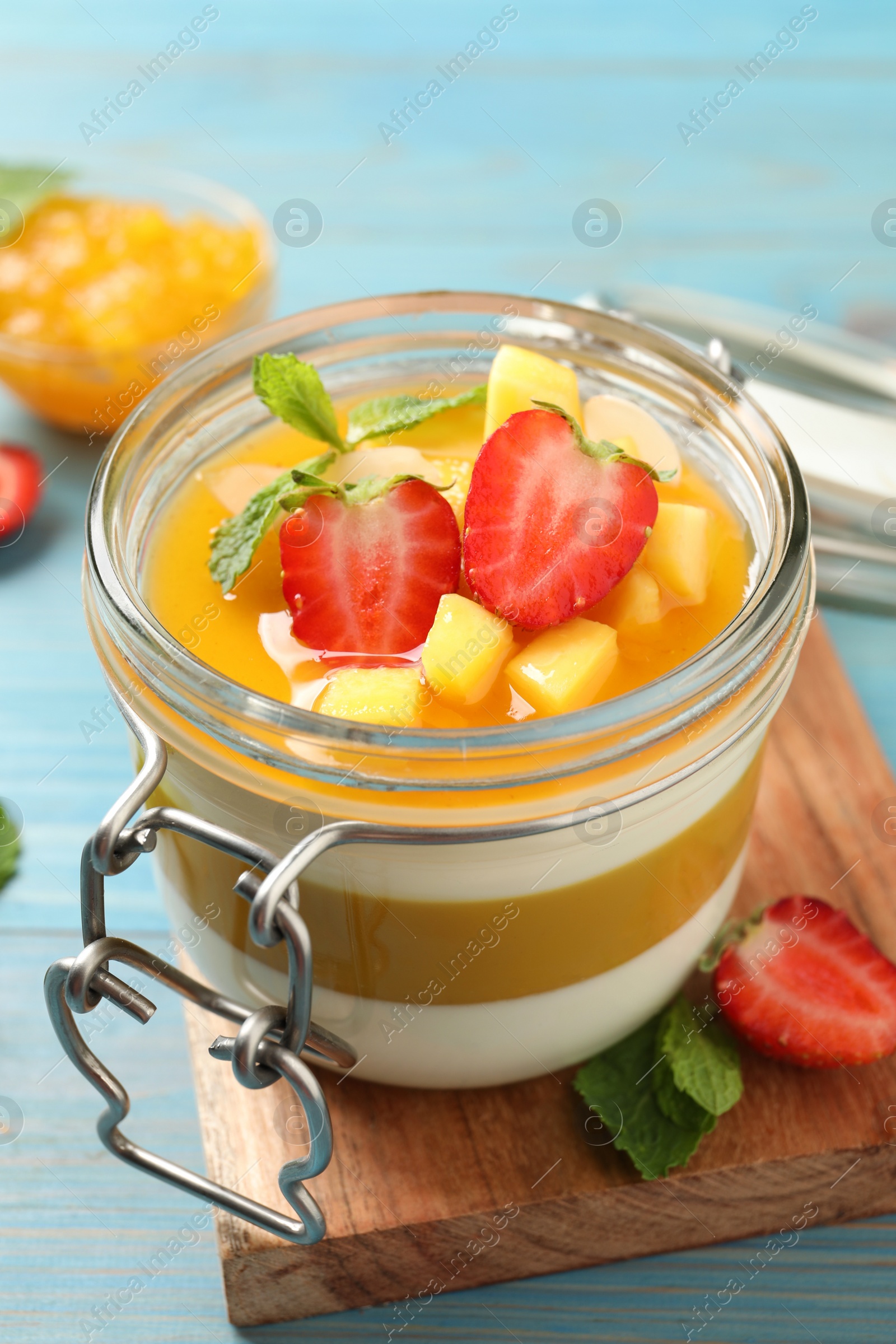 Delicious panna cotta with mango coulis and fresh fruit pieces on light blue wooden table Photo of Delicious panna cotta with mango coulis and fresh fruit pieces on light blue wooden table