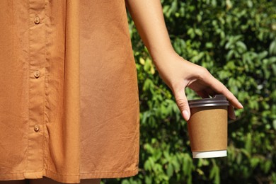Woman holding takeaway cardboard coffee cup with plastic lid outdoors, closeup Photo of Woman holding takeaway cardboard coffee cup with plastic lid outdoors, closeup