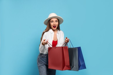 Excited young woman with shopping bags on light blue background Photo of Excited young woman with shopping bags on light blue background