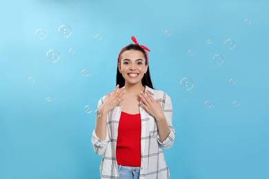 Young woman having fun with soap bubbles on light blue background Photo of Young woman having fun with soap bubbles on light blue background