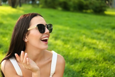 Beautiful young woman wearing stylish sunglasses in park. Space for text Photo of Beautiful young woman wearing stylish sunglasses in park. Space for text