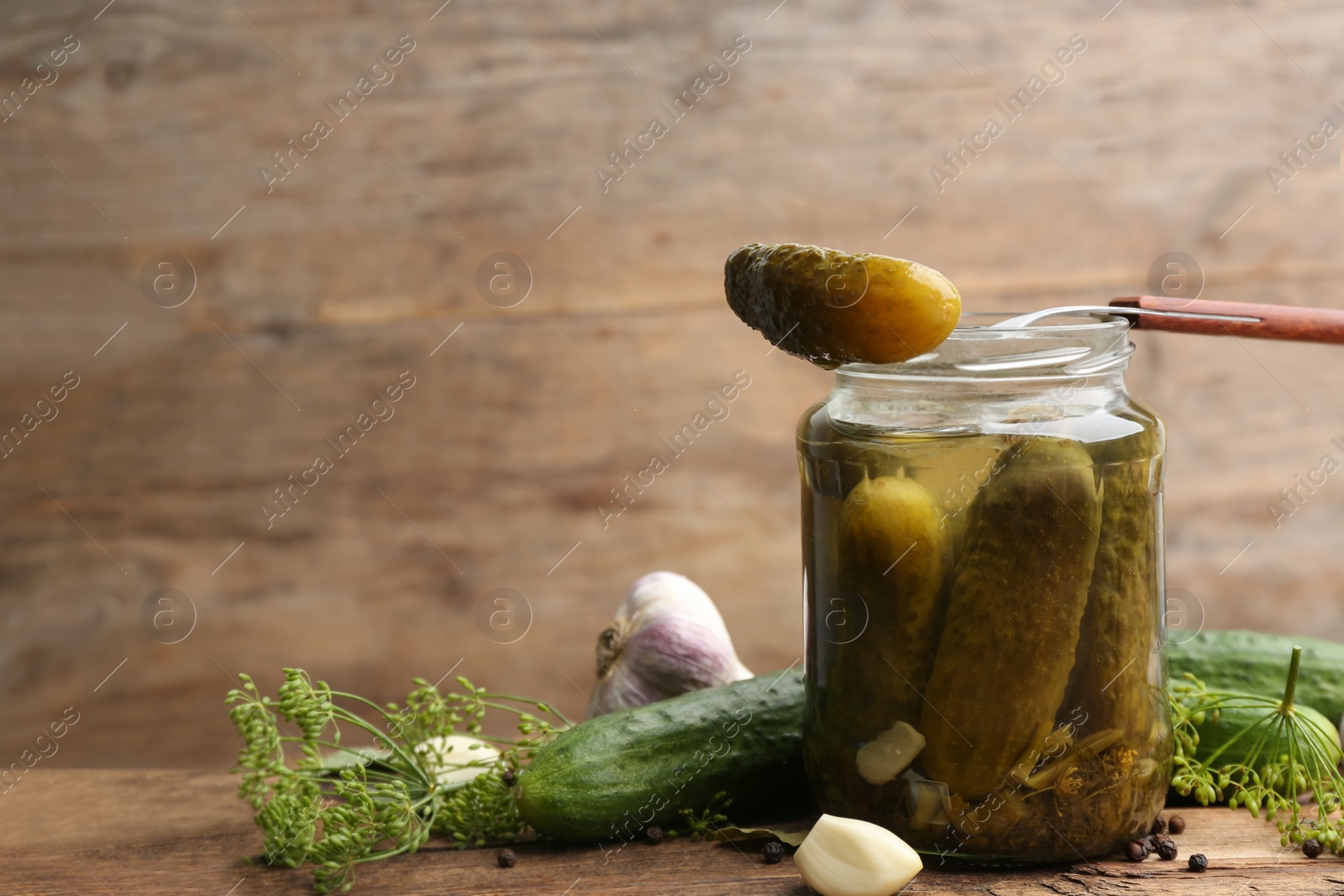 Glass jar of pickled cucumbers and ingredients on wooden table. Space for text Photo of Glass jar of pickled cucumbers and ingredients on wooden table. Space for text
