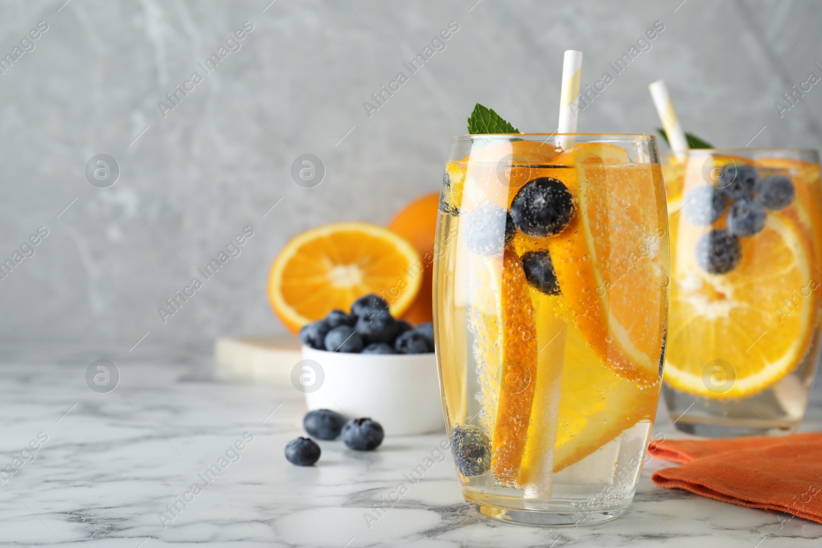Delicious orange lemonade with soda water, mint and blueberries on white marble table, space for text. Fresh summer cocktail Photo of Delicious orange lemonade with soda water, mint and blueberries on white marble table, space for text. Fresh summer cocktail