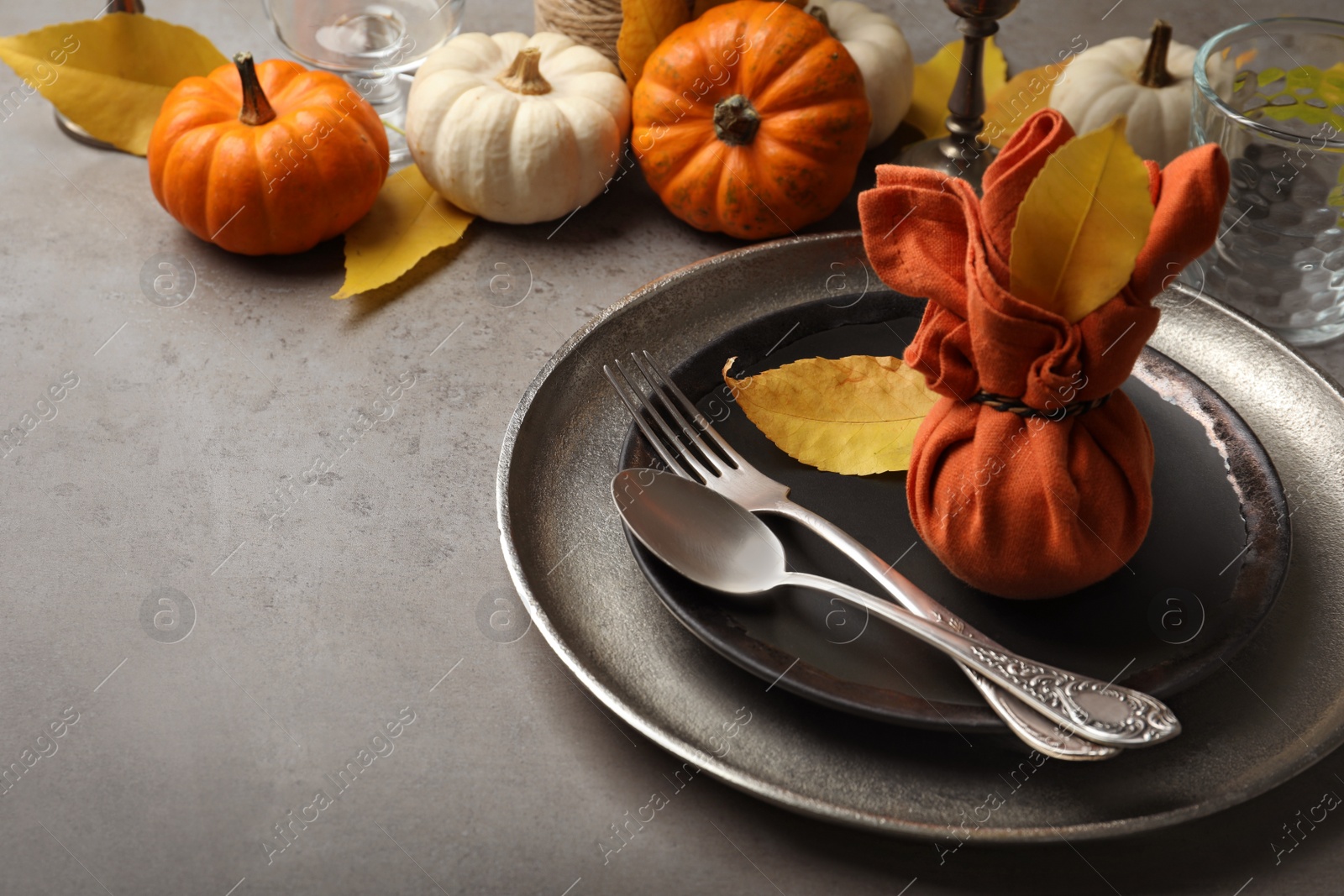 Seasonal table setting with pumpkins and autumn leaves on grey background. Space for text Photo of Seasonal table setting with pumpkins and autumn leaves on grey background. Space for text