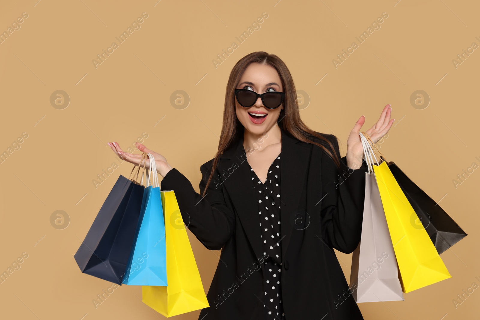 Stylish young woman in sunglasses with shopping bags on beige background Photo of Stylish young woman in sunglasses with shopping bags on beige background
