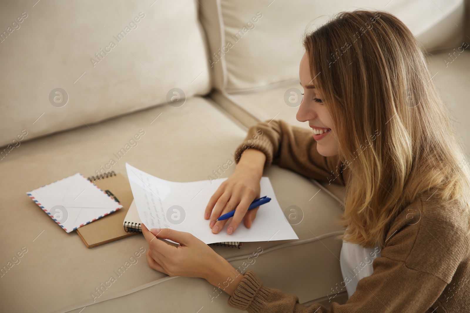Happy woman writing letter on sofa at home Photo of Happy woman writing letter on sofa at home