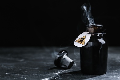 Open glass bottle of smoking poison with warning sign on black table. Space for text Photo of Open glass bottle of smoking poison with warning sign on black table. Space for text