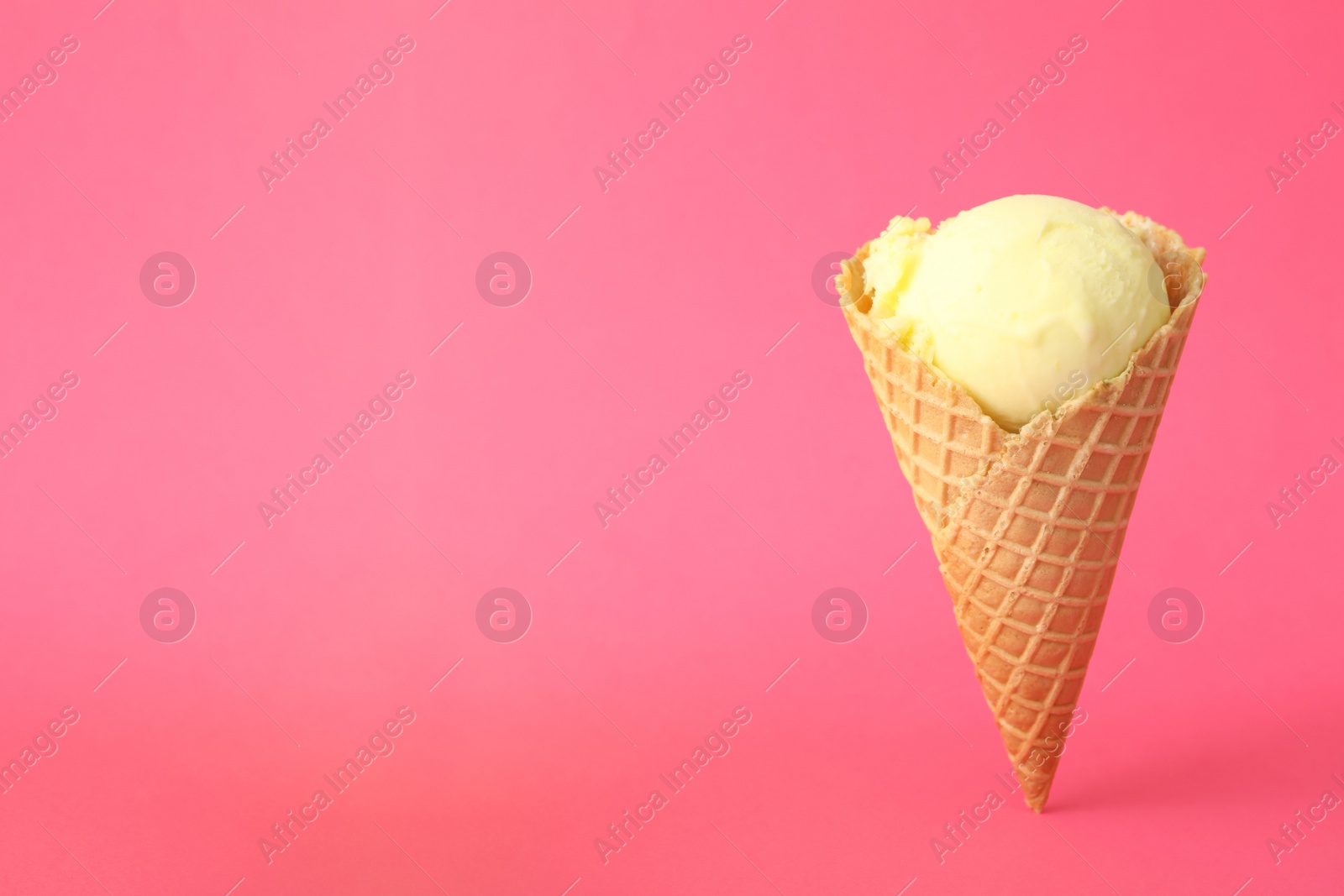 Delicious yellow ice cream in waffle cone on pink background. Space for text Photo of Delicious yellow ice cream in waffle cone on pink background. Space for text
