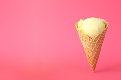 Delicious yellow ice cream in waffle cone on pink background. Space for text Photo of Delicious yellow ice cream in waffle cone on pink background. Space for text